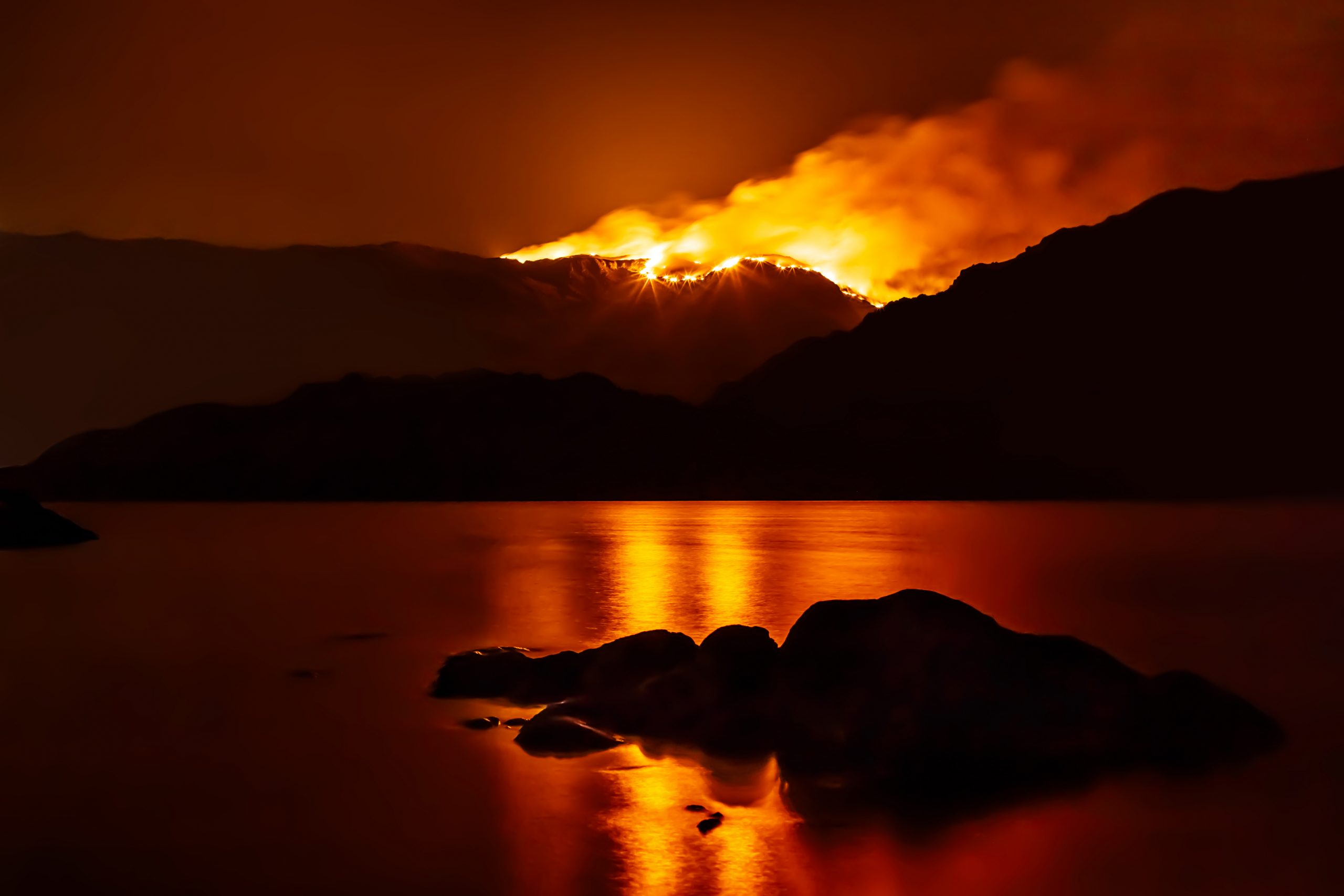 Forest fire at night reflecting in nearby lake. Drax