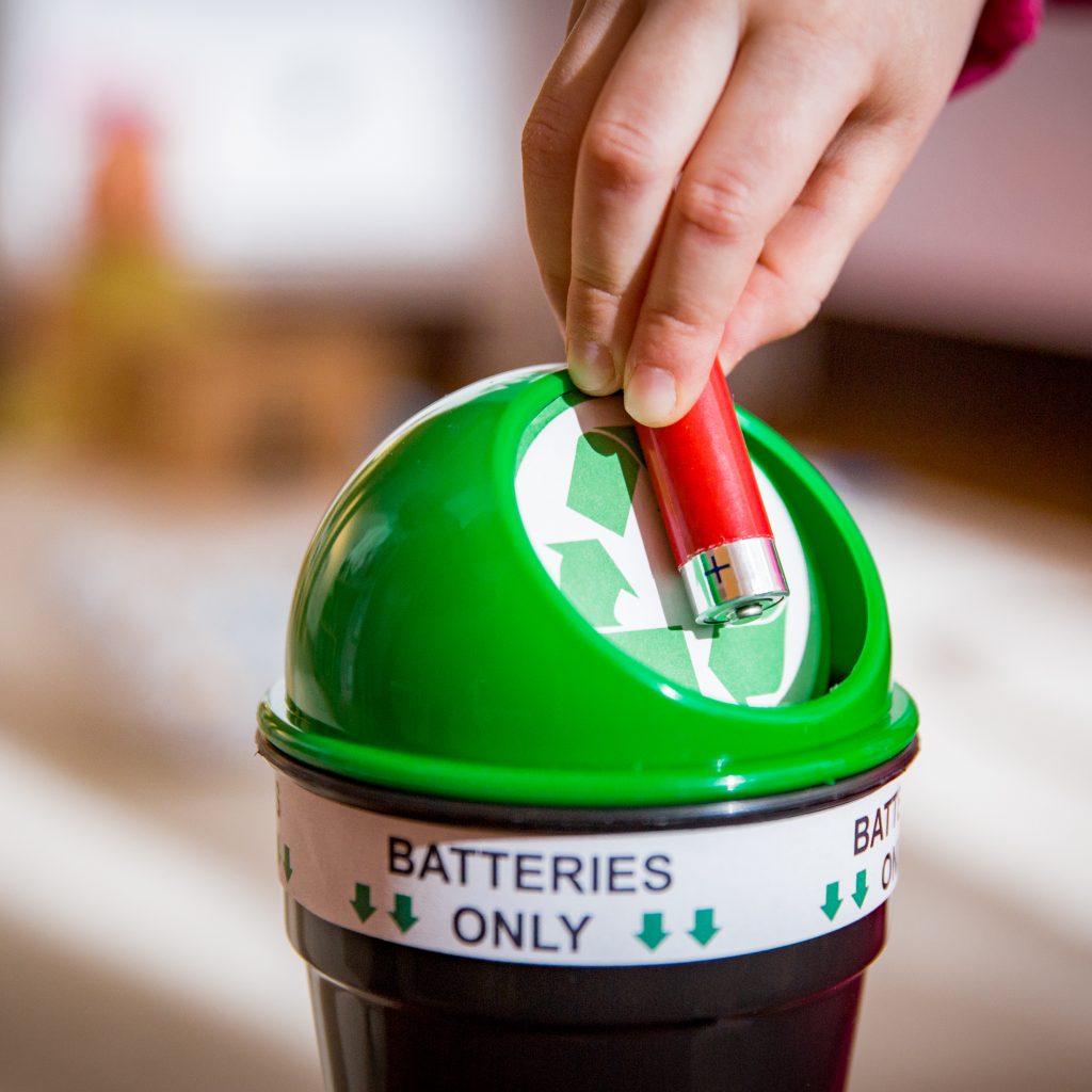 Little girl putting used batteries into recycling box at home. Child in ...